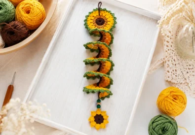 Crochet sunflower wind spinner pattern styled on a tray with yarn and crochet hook
