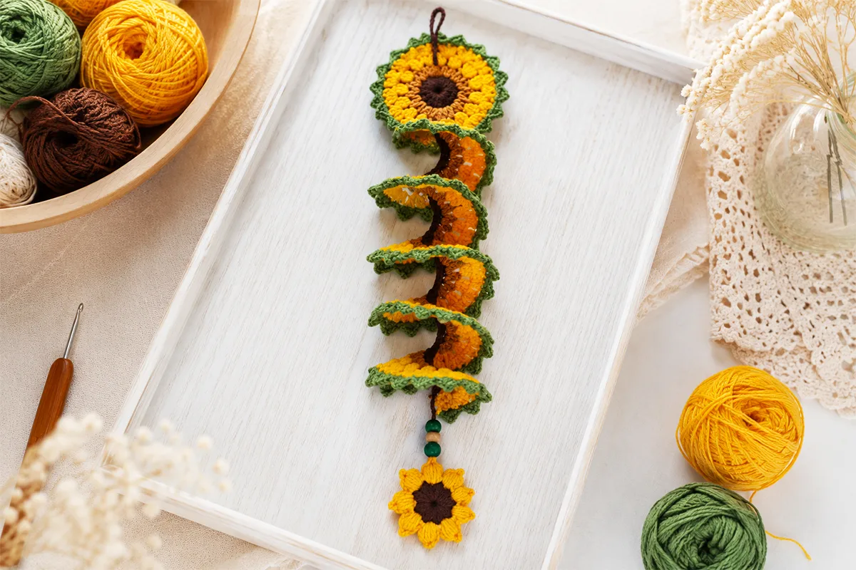 Crochet sunflower wind spinner pattern styled on a tray with yarn and crochet hook