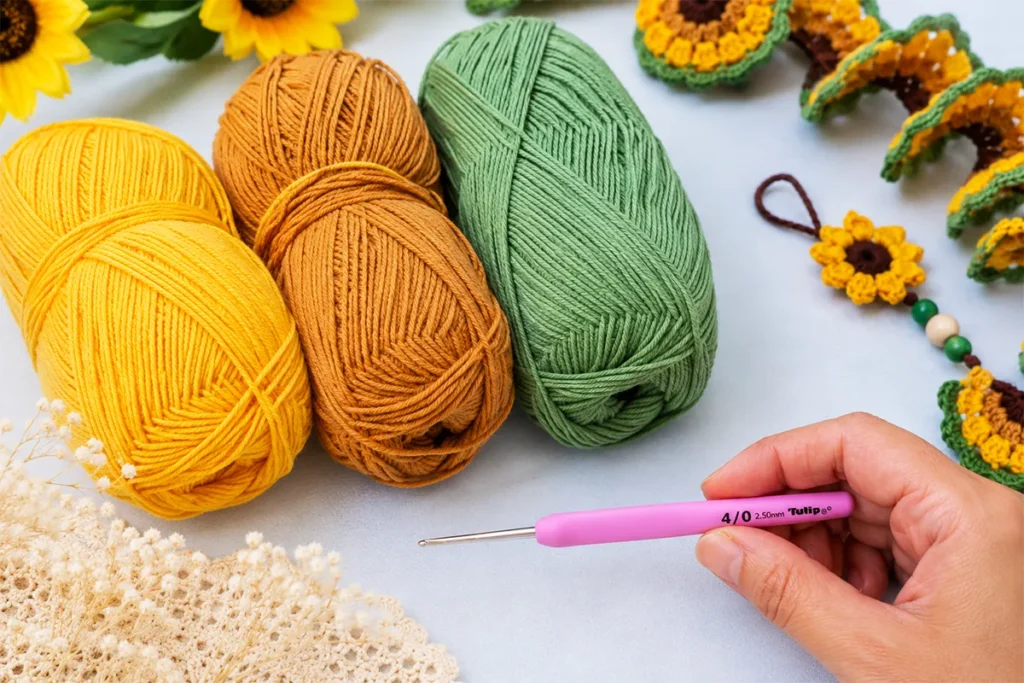 Materials for crochet sunflower wind spinner pattern including cotton yarn in yellow, brown, and green with a 2.5 mm crochet hook