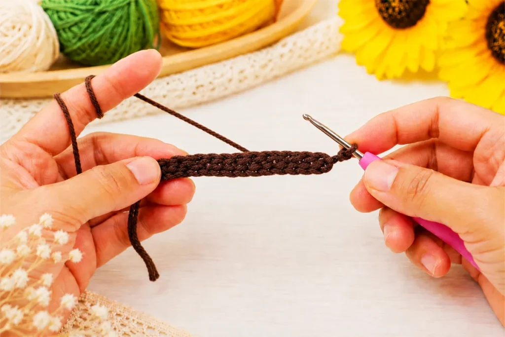 Hands working row 1 half double crochet stitches on a brown crochet strip for a crochet sunflower wind spinner pattern