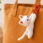 White crochet cat keychain with pink ears and a red star clasp hanging from a brown tote bag.