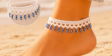 White crochet evil eye anklet with dangling blue charms displayed on a soft neutral craft table with cotton yarn and a crochet hook.