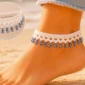 White crochet evil eye anklet with dangling blue charms displayed on a soft neutral craft table with cotton yarn and a crochet hook.