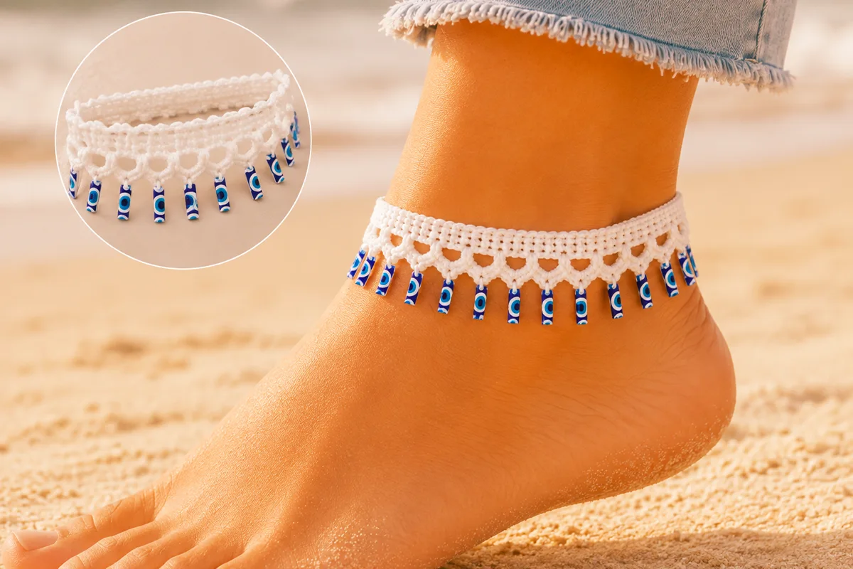 White crochet evil eye anklet with dangling blue charms displayed on a soft neutral craft table with cotton yarn and a crochet hook.