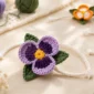 Purple crochet pansy bracelet with green leaves, white cord, and star-shaped ends arranged with colorful crochet flower bracelets and yarn.