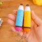 Two crochet pencil keychains in blue and yellow held in a hand with school supplies in the background