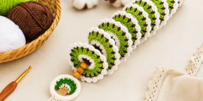 Green, white, and brown crochet wind spinner with wooden beads and a small tree charm, displayed with matching yarn balls and a crochet hook.