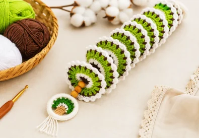 Green, white, and brown crochet wind spinner with wooden beads and a small tree charm, displayed with matching yarn balls and a crochet hook.
