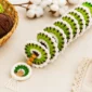 Green, white, and brown crochet wind spinner with wooden beads and a small tree charm, displayed with matching yarn balls and a crochet hook.