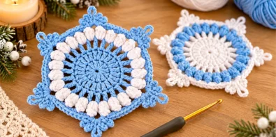 Crochet snowflake coaster with blue center, white popcorn stitches and a reversed-color coaster in the background