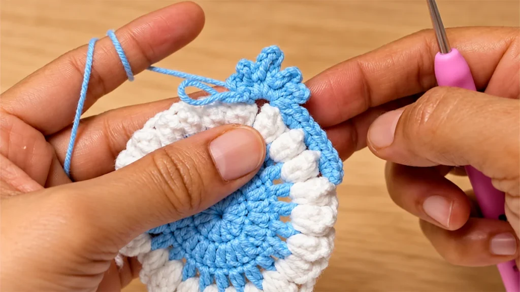 Close-up of blue chain-loop snowflake point edging beside the raised white popcorn stitches.