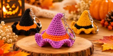 Purple crochet witch hat keychain with an orange band and curved tip displayed in a warm autumn setting.