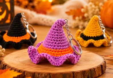 Purple crochet witch hat keychain with an orange band and curved tip displayed in a warm autumn setting.