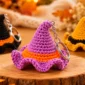 Purple crochet witch hat keychain with an orange band and curved tip displayed in a warm autumn setting.
